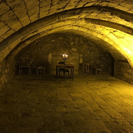 An arched stone room with a table and chairs, lit by a single candle. 4