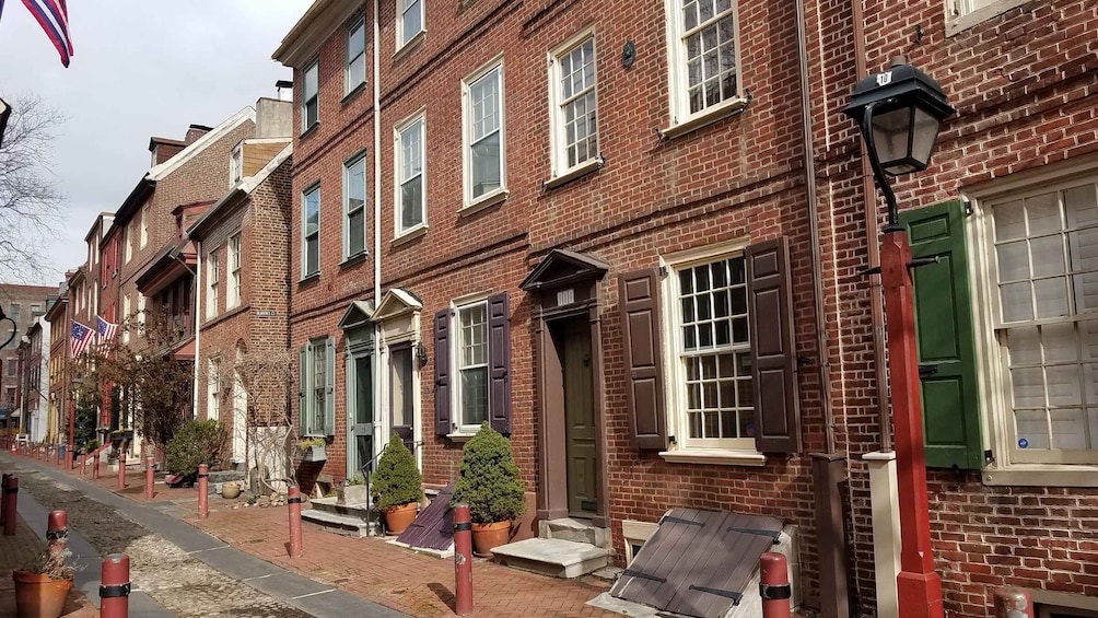 A row of red brick townhouses with green shutters, a street lamp, and American flags. 1