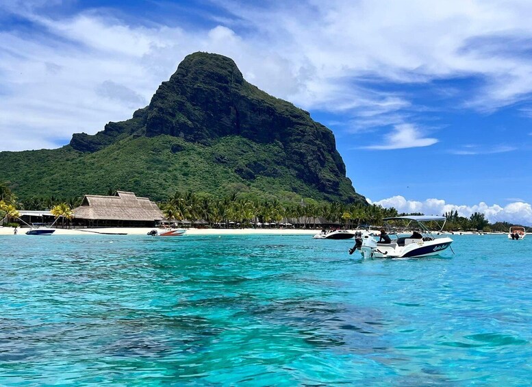A tropical island with clear turquoise waters, a large mountain, and several boats. 1