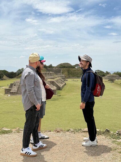 Two people standing on a grassy area with ancient ruins in the background. 1