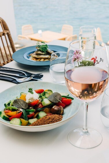 A table with a plate of salad and a glass of rosé wine, with a view of the sea in the background. 1