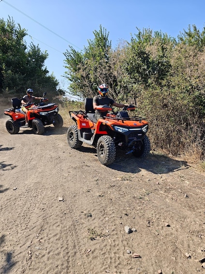 Two orange off-road vehicles on a dirt path with vegetation on the sides. 3