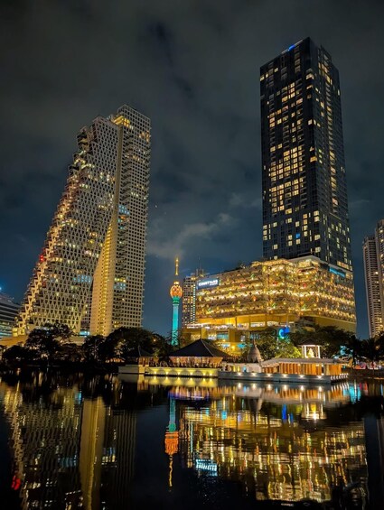 A cityscape at night with illuminated buildings, a mosque with a green and blue minaret, and a waterfront reflecting the lights. 4