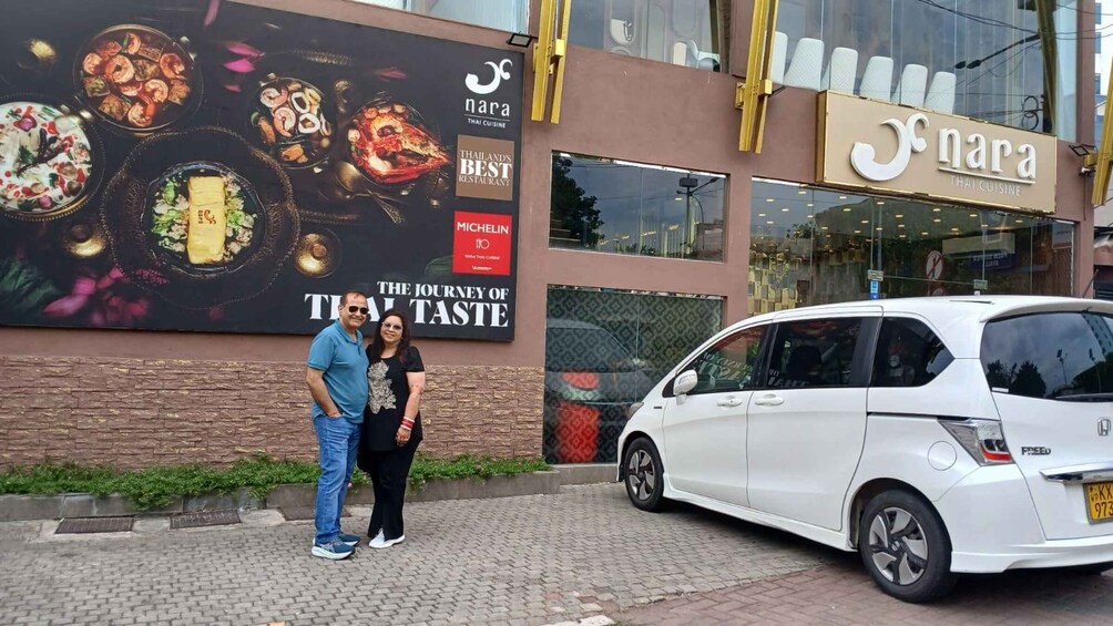 A couple standing in front of a Thai restaurant with a large food advertisement on the wall. 3