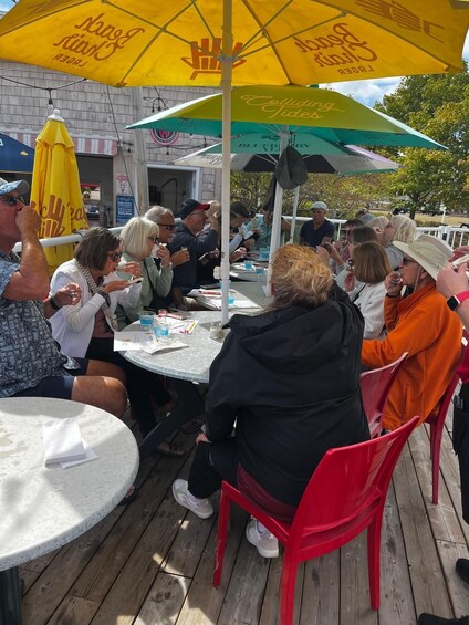 A group of people sitting at round tables under umbrellas at an outdoor event. 3