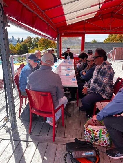 A group of people seated at a long table under a red canopy, outdoors. 5