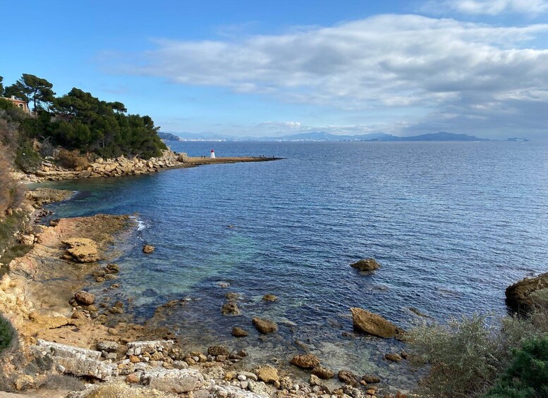 A coastal landscape with rocky shores, clear blue sea, and distant mountains. 2