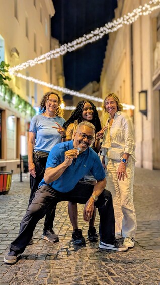 A group of people posing in a cobblestone street at night with string lights overhead. 1