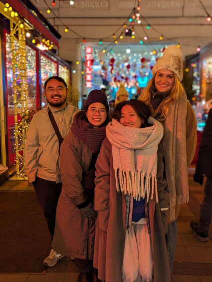 A group of people standing on a street at night, with illuminated decorations and buildings in the background. 5