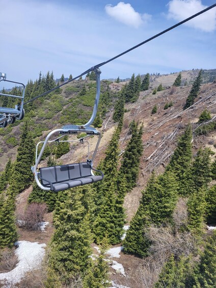 A ski lift chair suspended over a forested mountain slope with patches of snow. 4