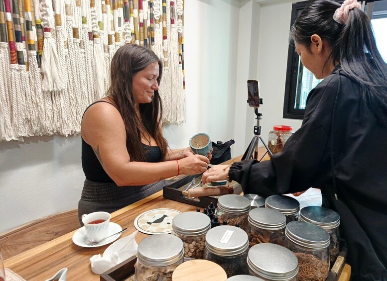 Two people at a table with jars of coffee beans, a camera on a tripod, and a wall with macramé. 4