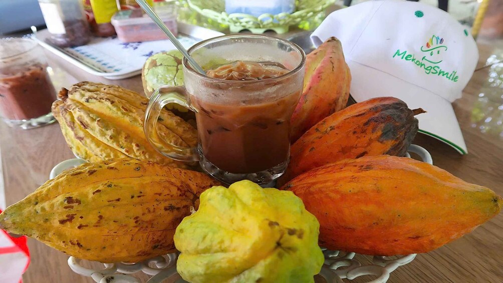 Un vaso de café helado, una gorra blanca con una carita sonriente y diversas frutas en un plato. 3