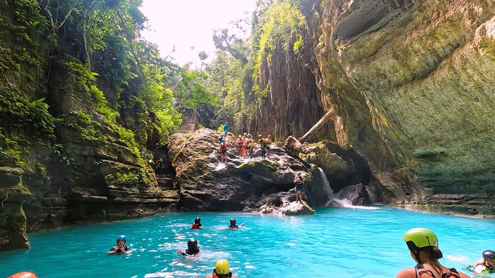 A group of people swimming in a turquoise pool surrounded by rocky cliffs and lush greenery. 3