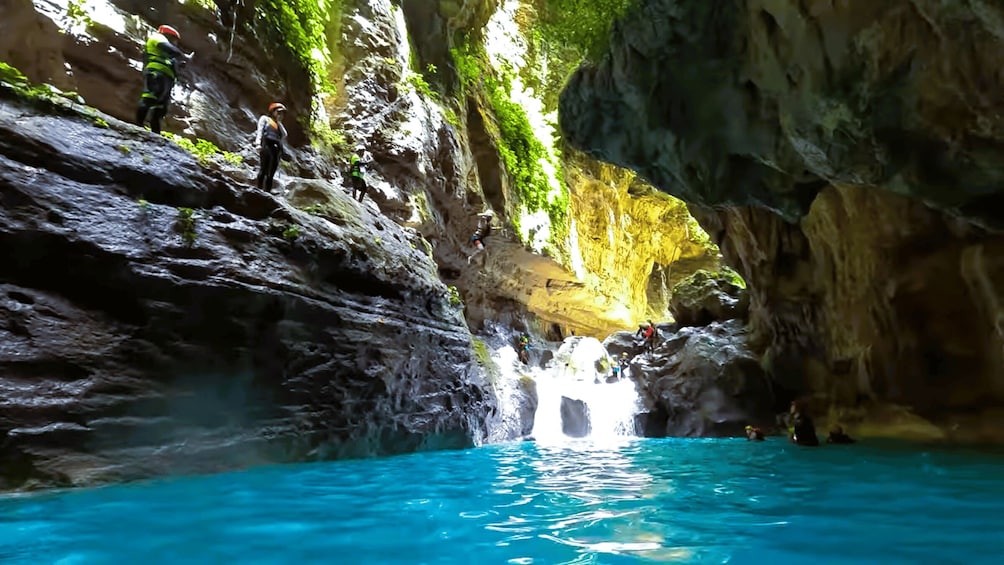 A cave with a waterfall and clear blue water. 4