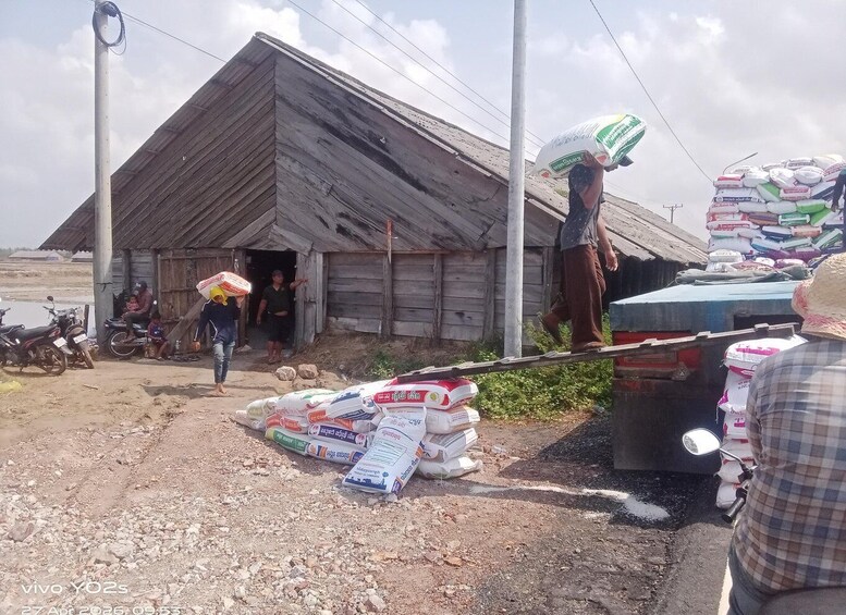 A rural scene with a wooden building, people carrying goods, and bags of fertilizer. 4