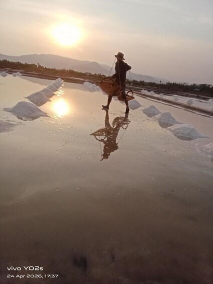 A person walking on a reflective surface with snow piles, mountains in the background, and a sunset. 5