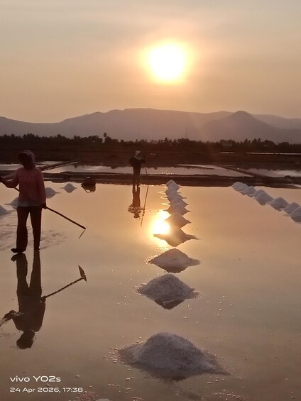 Two people walking on a reflective surface with mountains in the background and the sun setting. 3