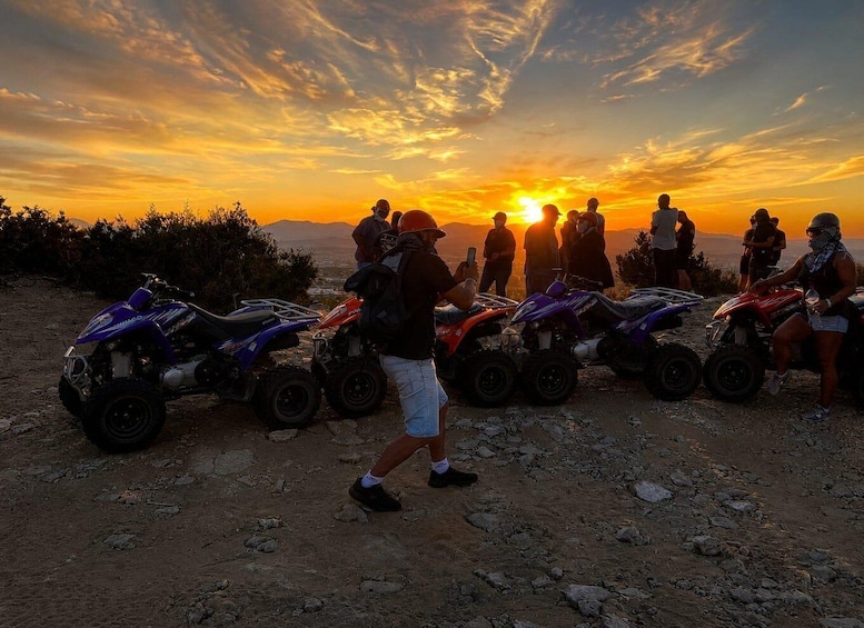 A group of people at sunset with ATVs parked on a rocky terrain. 2