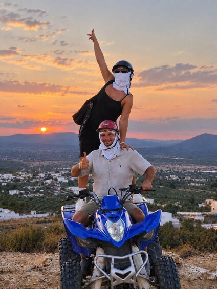 A person riding a blue quad bike with a helmet and a white cloth around the neck, giving a thumbs up. 3