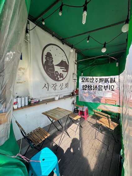 A tent with a table and chairs, a sign with Korean text, and a logo on the wall. 5