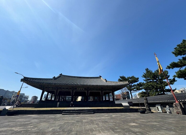 A traditional Korean pavilion with a tiled roof, surrounded by a paved area and trees. 1