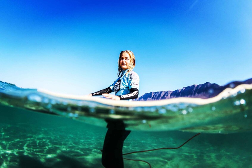A person surfing on a wave with clear water and mountains in the background. 1
