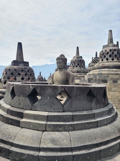 A stone Buddha statue surrounded by traditional Indonesian stupa structures. 4