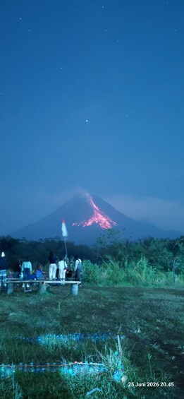 A group of people observing a volcano with glowing lava at night. 2