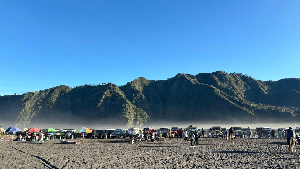 A beach with vehicles and people, and a mountain range in the background. 1