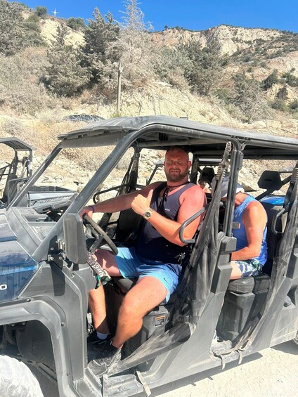 A person driving a 4x4 vehicle on a sandy terrain with sparse vegetation and rocky hills in the background. 2