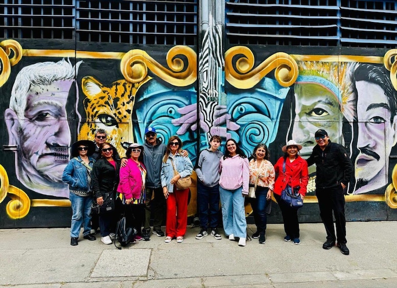 A group of people standing in front of a colorful mural with abstract designs and portraits. 3