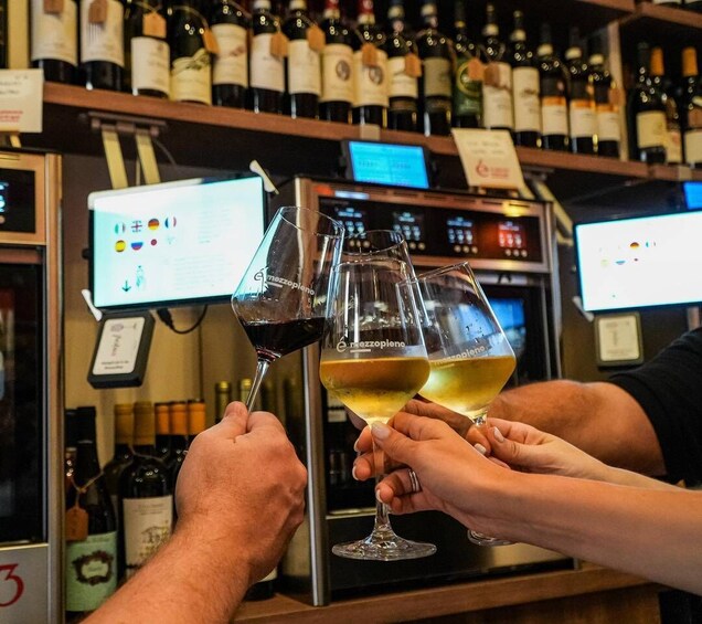 A bar with people toasting with wine glasses, a computer monitor, and shelves of wine bottles. 1