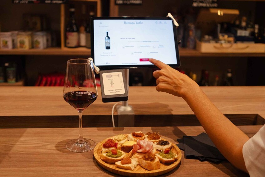 A person pointing at a digital menu on a tablet, with a glass of red wine and a plate of appetizers on the table. 2