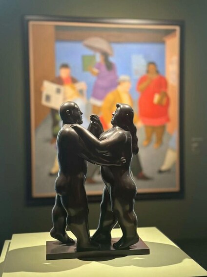 A sculpture of two figures embracing, with a framed painting in the background. 2