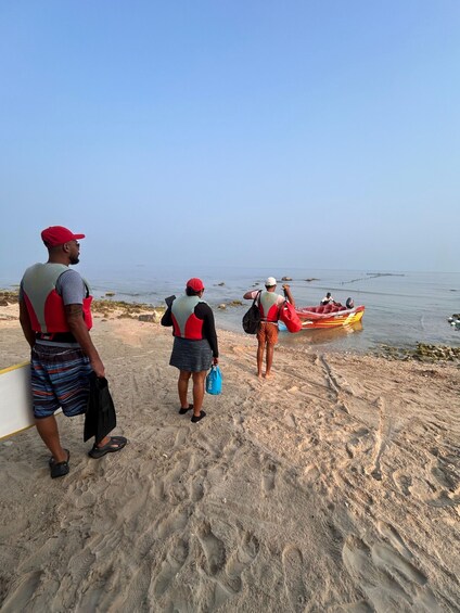 People on a sandy beach, some wearing life jackets, a red inflatable boat in the water, and footprints in the sand. 4