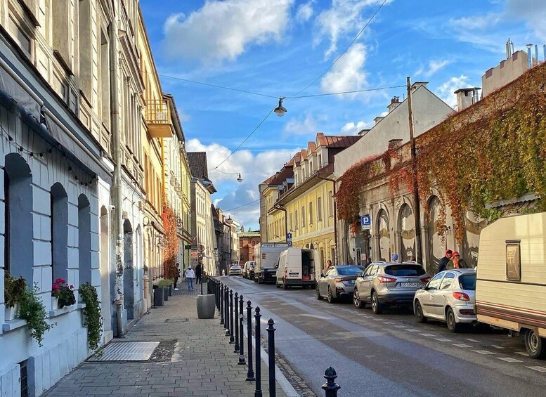 A narrow urban street lined with historic buildings, parked cars, and a tram. 5