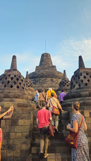 Tourists ascending stone steps towards a large, pyramid-like structure with a flagpole on top. 2