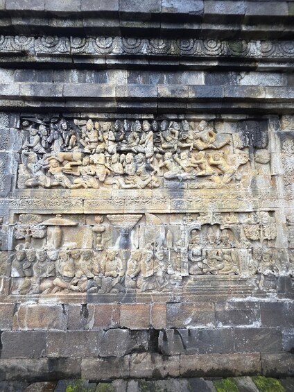 A detailed stone carving depicting a historical scene with multiple figures, including seated and standing individuals, some holding objects. 3