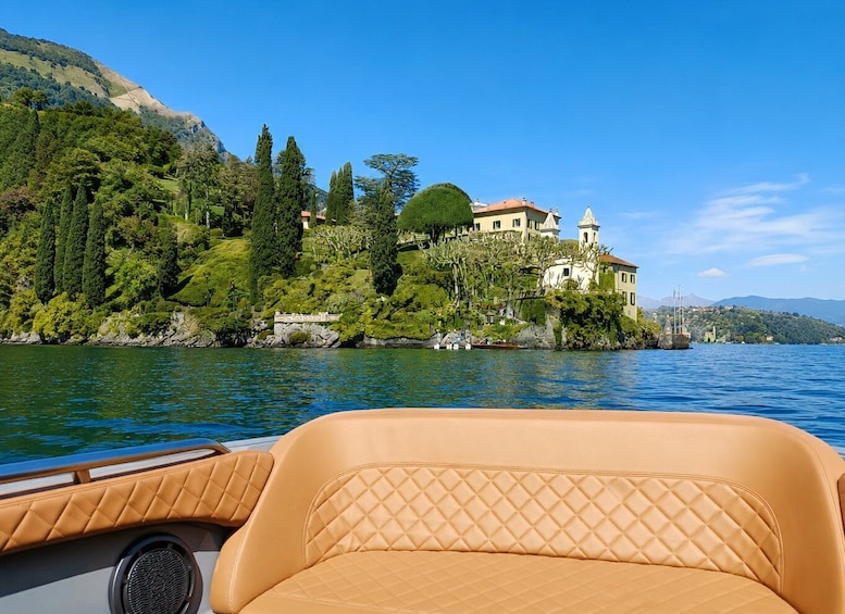 A boat with tan leather seats, a calm lake, and a hillside with a large house and trees. 2