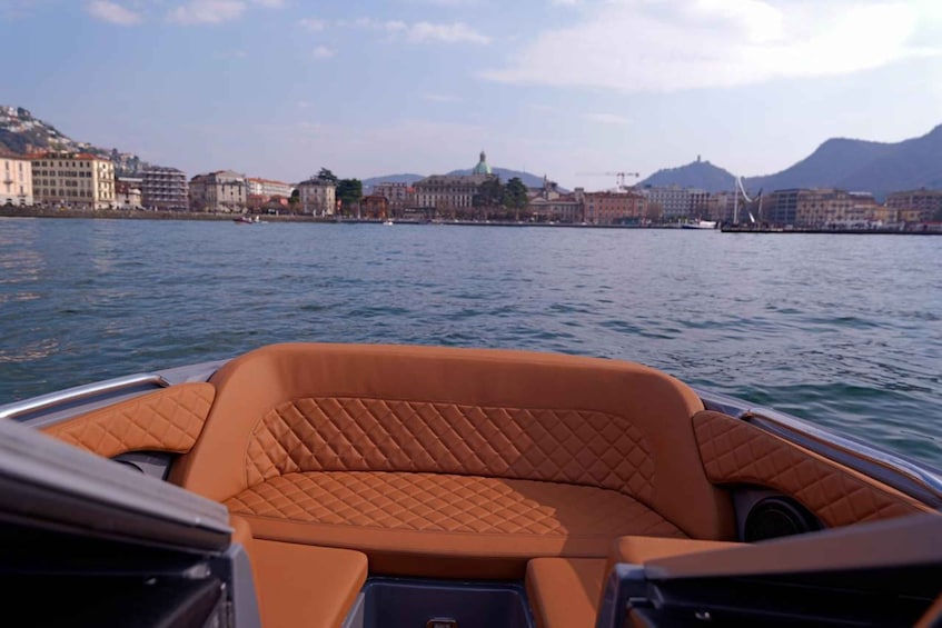 A boat with a brown cushioned interior, water, and a cityscape with buildings and mountains in the background. 5