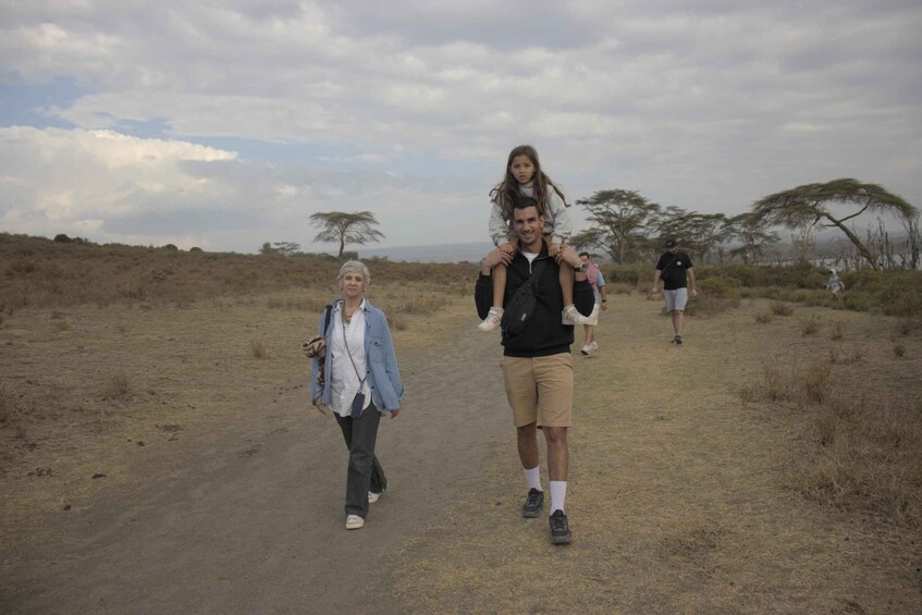 A group of people walking on a dirt path in a savannah landscape with sparse trees and a cloudy sky. 3