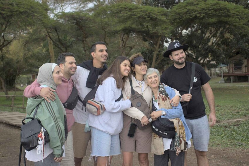 A group of people standing in a park with trees and a wooden structure in the background. 5