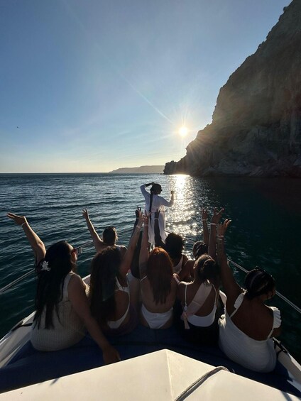 A group of people on a boat facing a cliff by the sea with the sun setting in the background. 5