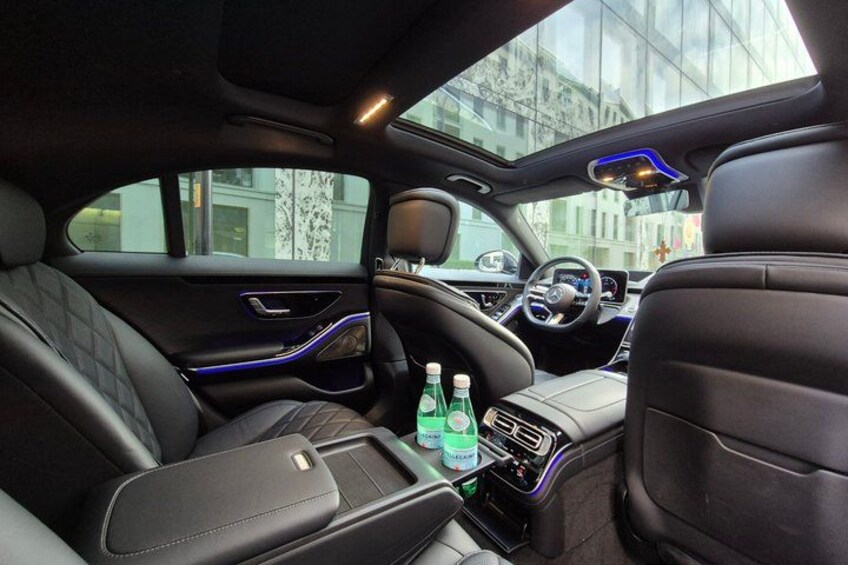 A luxury car interior with leather seats, a sunroof, and a center console with bottles. 3