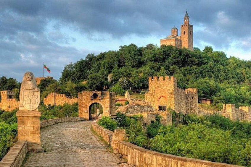 Een historisch stenen fort met een opvallende toren, omgeven door weelderige begroeiing en een geplaveid pad. 1