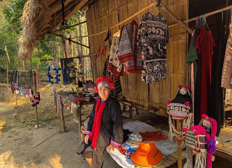 Una persona vestida con atuendo tradicional frente a una estructura de madera con textiles y joyería expuestos. 3
