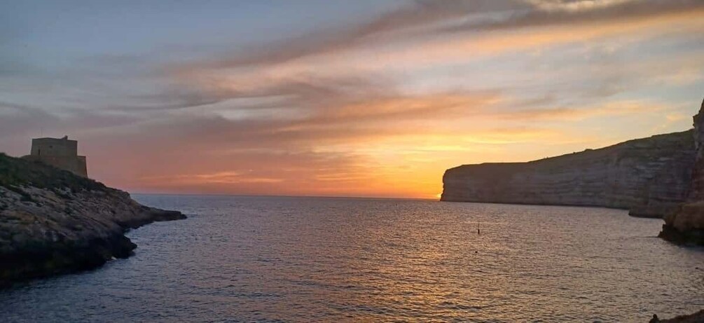A sunset over a coastal landscape with cliffs and a small building on the left. 4