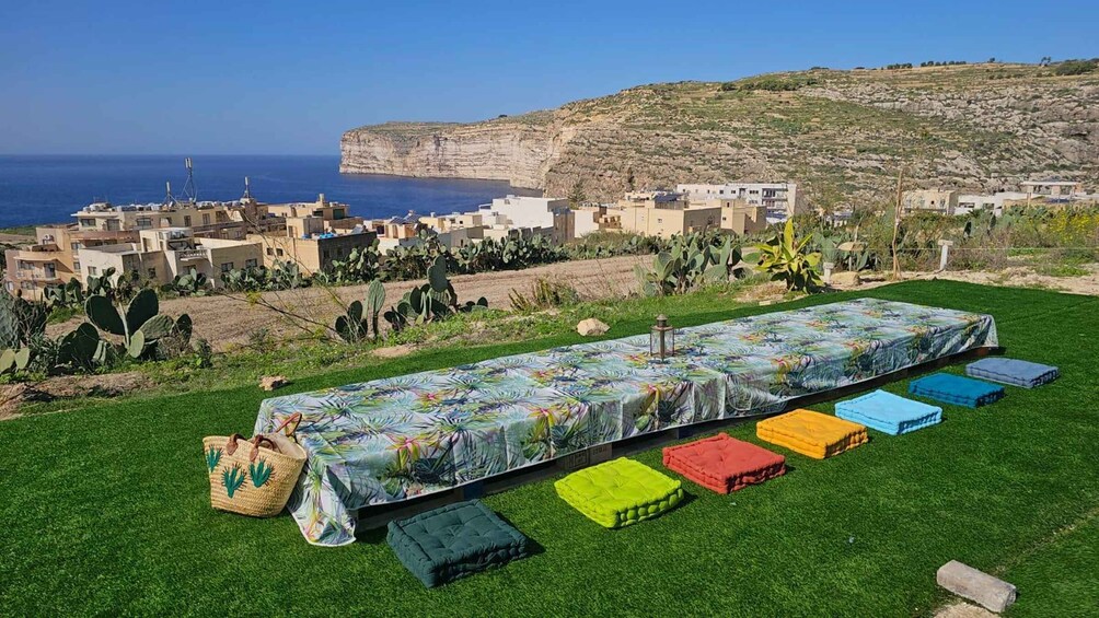A covered outdoor space with colorful cushions and a table, overlooking a coastal village and cliffs. 2