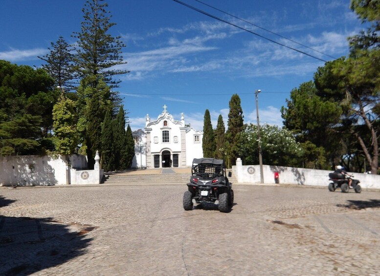 A paved street leading to a white church with a cross on top, surrounded by trees and a clear blue sky. 4
