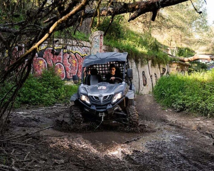 A vehicle navigating a muddy path in a forested area with graffiti on the wall. 1
